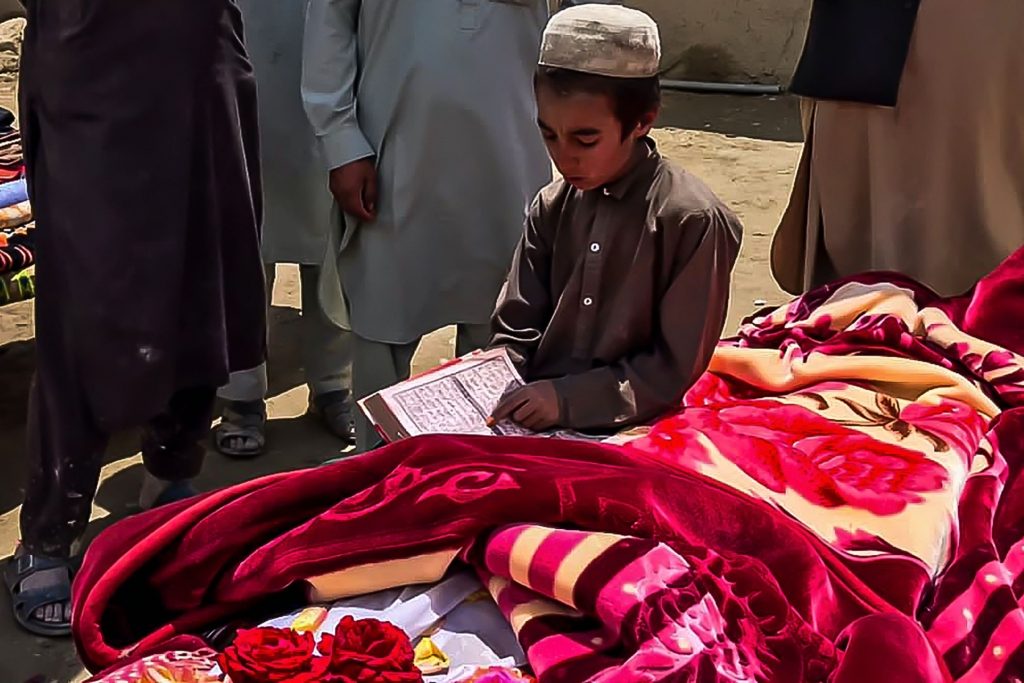 طفل أفغاني يقرأ القرآن أمام جثة أحد الضحايا